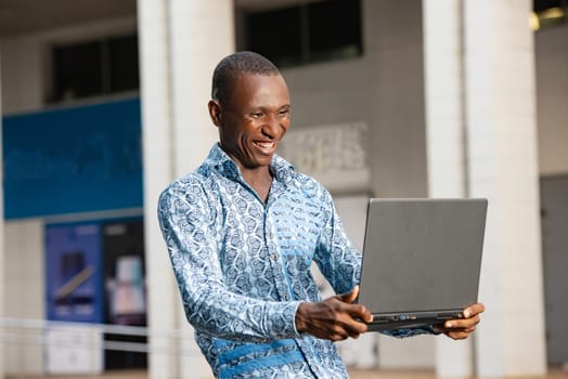 young african man standing celebrating success on the street looking at his laptop in hand