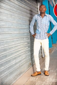 African adult man wearing a shirt and jeans standing on the street thinking about something by putting his hands on his hip