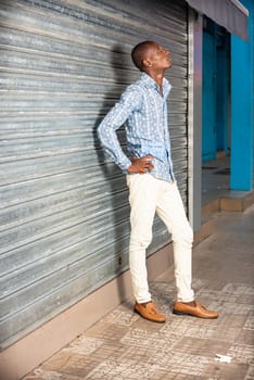 African adult man wearing a shirt and jeans standing in the street thinking about something