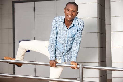 young man in traditional clothes jumping iron bar and looking at camera smiling.
