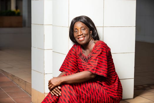 beautiful mature woman sitting near a wall in traditional dress looking at the camera smiling.