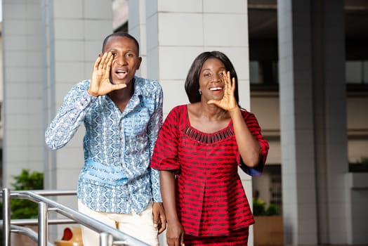 two business people standing in traditional clothes beckoning to someone smiling.