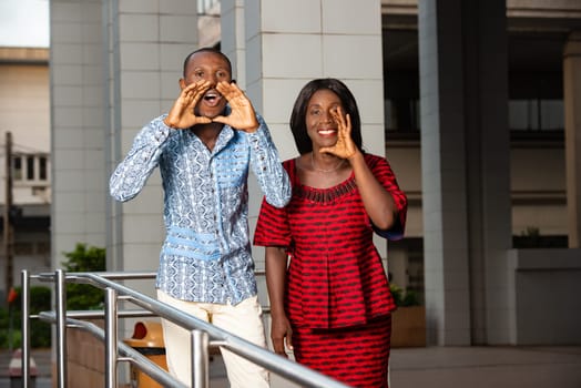 two business people standing in traditional clothes beckoning to someone smiling.