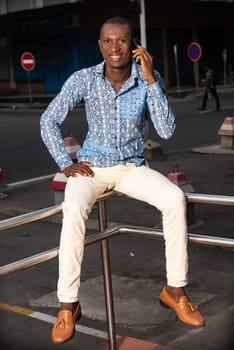 young african man sitting on an iron in the street is communicating with his mobile phone in souraint
