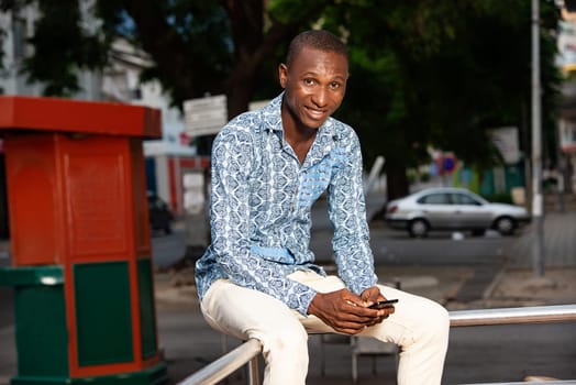 handsome adult african man sitting in the street using his mobile phone
