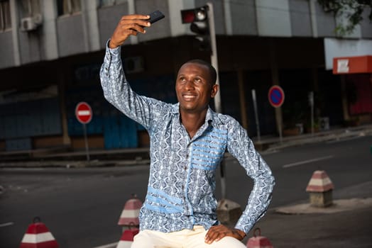 Young handsome african man sitting in the street and calling by mobile phone or video call while smiling