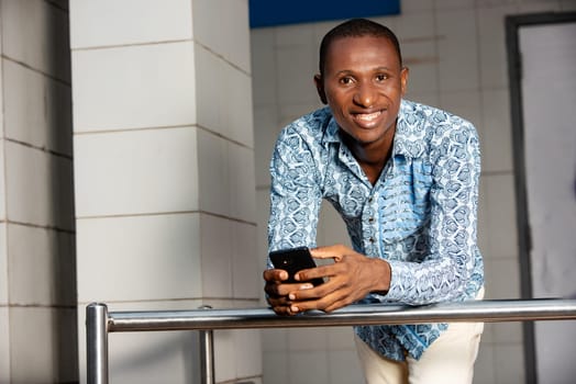 handsome african adult man holding in hand a mobile phone while smiling