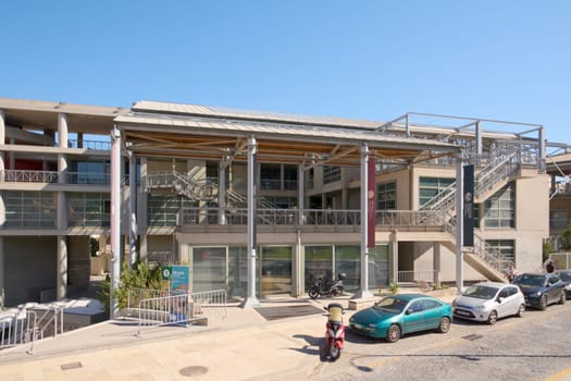Crete.Greece - april 13, 2025: Heraklion's cultural congress center features contemporary lines, metallic textures, and glass panels, surrounded by parked vehicles and clear blue skies.