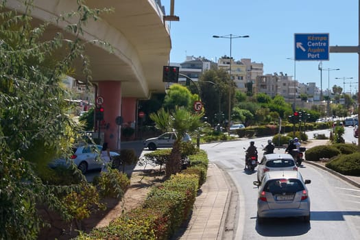 Crete.Greece - april 13, 2025: A busy road in Heraklion featuring a prominent traffic sign pointing toward the port, framed by urban elements and a clear blue sky.