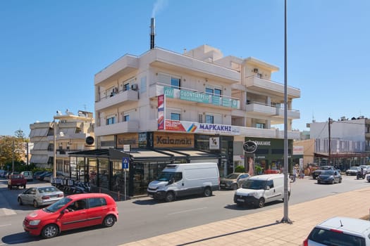 Crete.Greece - april 13, 2025: A vibrant street in Heraklion featuring a multi-story building with shops and restaurants, busy with parked cars and Greek signage under sunny skies.