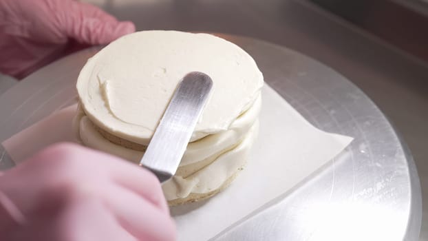 Female professional hands levels cream on baked sponge cake using metallic pastry scraper. Dessert decor. Pastry decoration. High quality