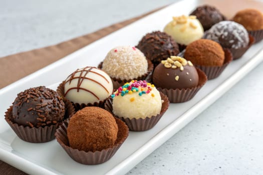 Assorted handmade truffles displayed on a white platter showcase a variety of coatings, colors, and textures, creating an enticing treat perfect for any chocolate lover at a dessert event.