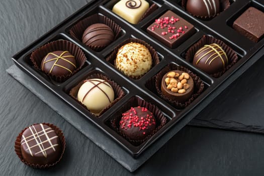 A collection of handmade chocolates displayed in an elegant black tray showcases a variety of flavors and designs. Each piece is uniquely crafted for a delightful tasting experience.