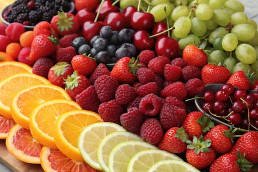 A colorful assortment of fresh fruits is beautifully arranged on a wooden surface. Bright oranges, red strawberries, juicy cherries, and green grapes come together for a healthy snack.