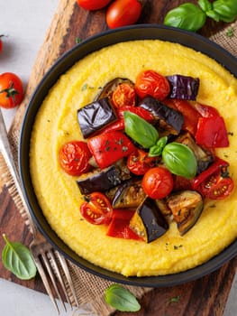 A bowl filled with creamy polenta is topped with vibrant roasted vegetables, including eggplant, bell peppers, and cherry tomatoes.