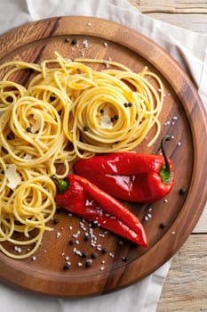 Spaghetti sits elegantly on a wooden platter, accompanied by vibrant red peppers and sprinkled with coarse salt and pepper. A rustic setup evokes warmth and culinary creativity.