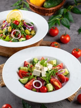 Two colorful salads featuring fresh tomatoes, cucumbers, red onions, and feta cheese served in white bowls. A lemon slice decorates one salad, enhancing the presentation.