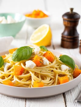A plate of spaghetti is presented with colorful butternut squash cubes and fresh basil leaves, set in a charming indoor dining area. The warm colors invite a sense of comfort and taste.
