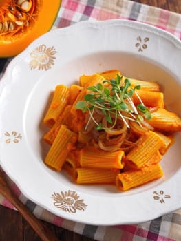 A delicious bowl of creamy pumpkin rigatoni is artfully presented on an elegant plate. Fresh microgreens and caramelized onions enhance the rich flavors.