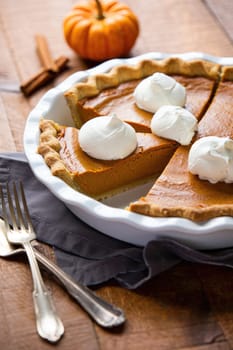 A freshly baked pumpkin pie sits on a wooden table, showcasing its rich orange filling and golden crust.