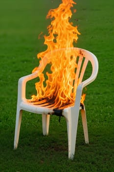 White chair set on fire in empty grassy field. Related idiom: 'burning bridges'. AI generation.