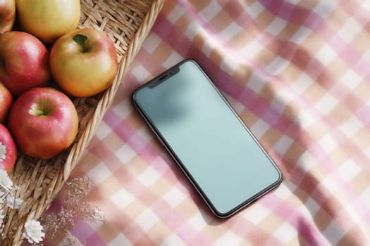 Smartphone on a pastel picnic blanket beside red and yellow apples in a wicker basket. Great for lifestyle branding, healthy food apps, seasonal outdoor promotions, and fresh organic content visuals