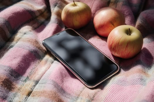 Modern smartphone placed on a soft checkered plaid with fresh apples. Perfect for technology mockups, organic product visuals, seasonal campaigns, and cozy lifestyle scenes