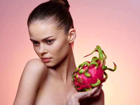 Beautiful young woman holding a fresh dragon fruit against a vibrant pink background in a stylish and modern stock photo