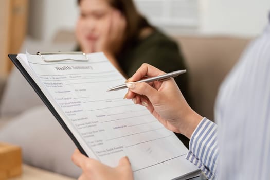 A therapist diligently observes a health summary while the client reflects on her feelings, highlighting the importance of thorough mental health assessments.
