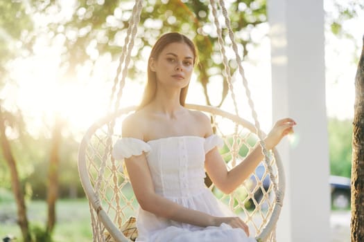 A serene young woman in a flowing white dress rests on a swing in a sunlit garden, embodying beauty and tranquility Perfect for concepts of nature and elegance
