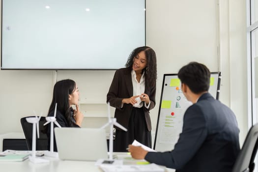During a collaborative meeting, a woman enthusiastically shares ESG performance metrics while her colleagues engage in the conversation, emphasizing teamwork and innovation.