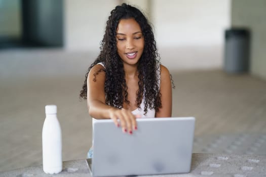 In a vibrant indoor space, a young woman with curly hair is engaged with her modern laptop, showcasing the importance of contemporary work culture and digital interaction in our lives