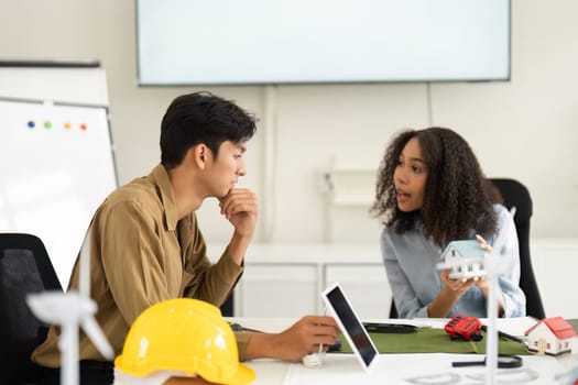 A vibrant discussion unfolds between professionals analyzing sustainable designs and strategies, with architectural models prominently displayed in their workspace.