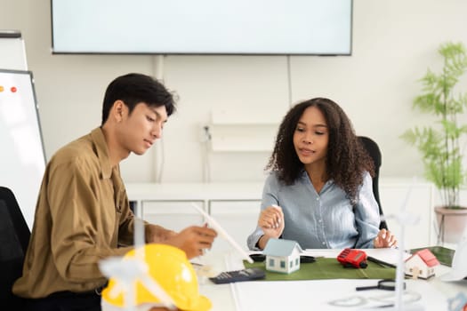 Two architects or engineers engaged in a discussion about sustainable architectural solutions, surrounded by models and tools in a contemporary office.