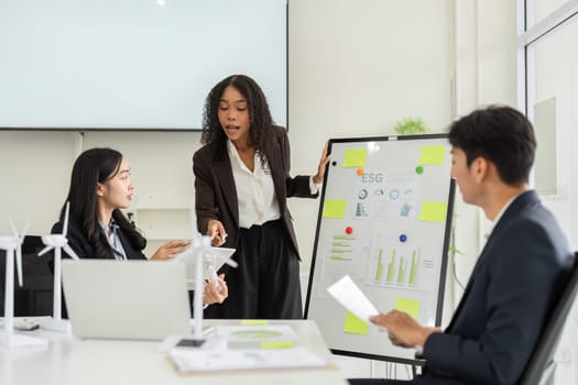 In a modern office, a woman presents key metrics related to ESG initiatives, fostering an open dialogue with her colleagues to drive sustainability efforts.