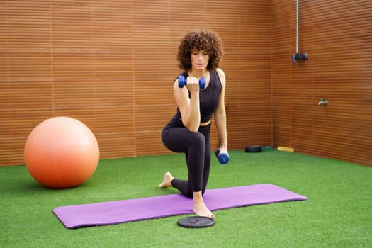 A fit and strong woman engages in an intense strength workout routine using dumbbells, showcasing her commitment to fitness and health in a vibrant, modern gym environment filled with equipment