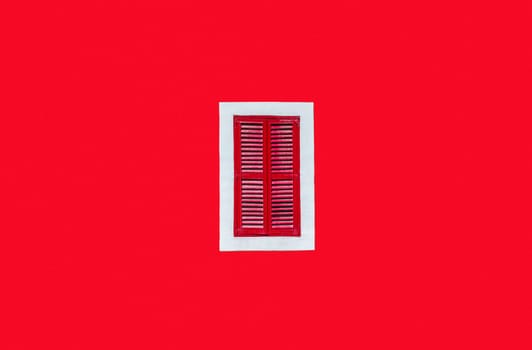 Plain red wall with a red window in a white frame in the middle of the shot