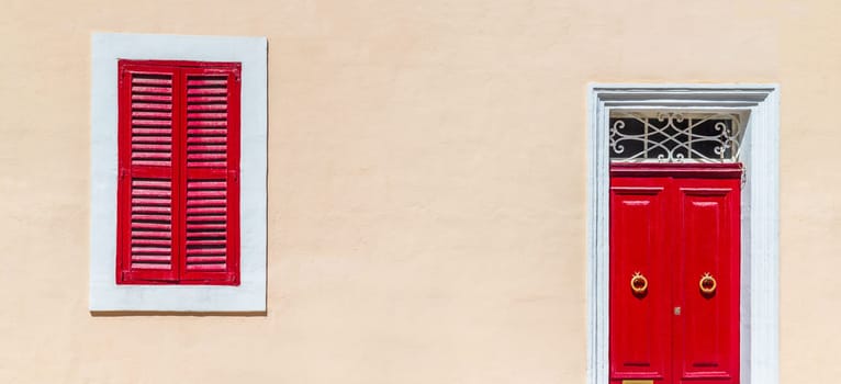 House facade colored in warm beige pastel color with bright red door and shuttered window, wide horizontal composition