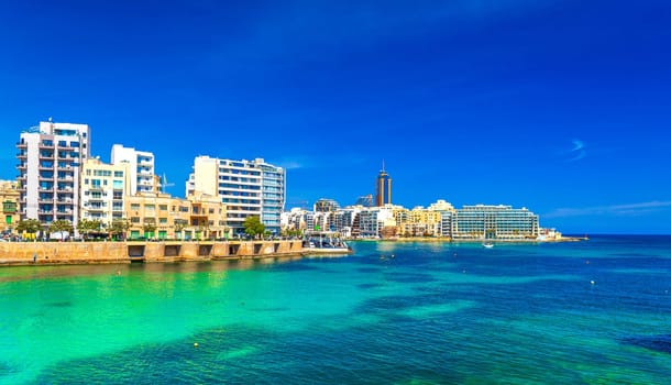 Cityscape of St Julian's Bay on a sunny day with clear blue skies and turquoise water, Malta