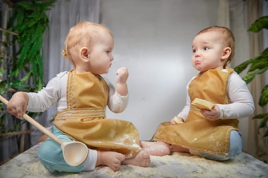 Two toddlers dressed as chefs delight in playful baking session, surrounded by flour and treats, sharing laughter and joy