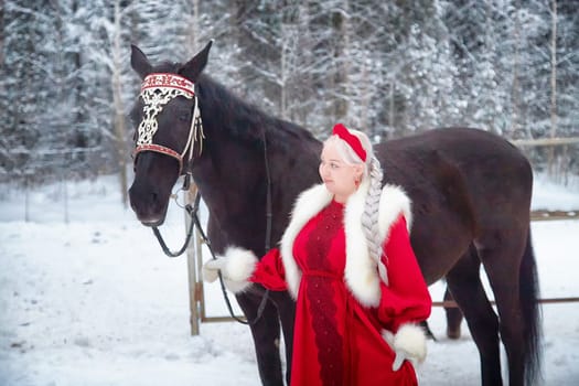 A girl in a traditional Russian outfit stands beside a decorated horse in a snowy landscape, celebrating Maslenitsa.