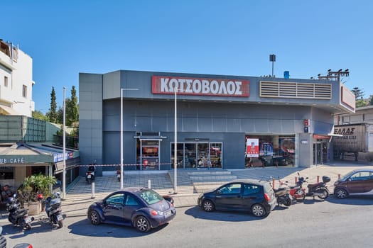 Crete.Greece - april 13, 2025: A busy urban street corner in Heraklion features a retail store named , a caf with outdoor seating CLUB CAFE, and other local businesses. Parked motorcycles.