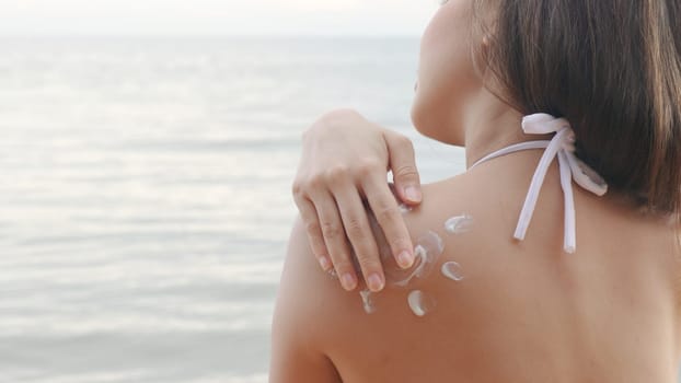 Beautiful Asian woman applying sun protection cream on tanned shoulder on the beach, sun Cream, Close up female in bikini using sunscreen lotion on back body before sunbathing