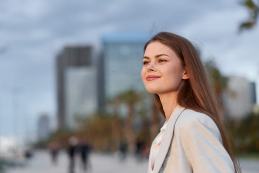 A confident woman dressed in a smart blouse, smiling against a backdrop of urban buildings at sunset, symbolizing professionalism and ambition in business.