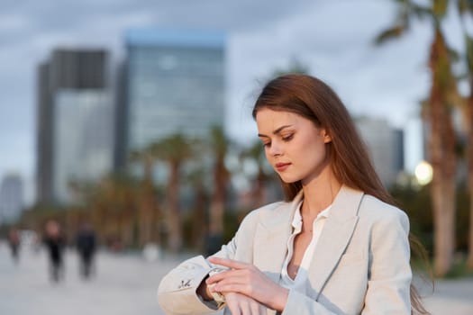 A focused business woman in a stylish suit looks at her watch against a modern city backdrop. Her confident demeanor reflects professionalism and determination, ideal for corporate themes.
