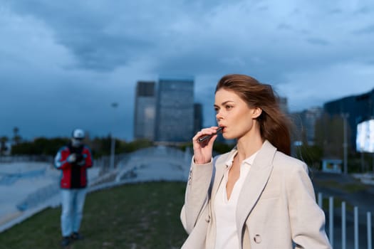 A confident woman in stylish business attire is outdoors, holding a pen and looking thoughtfully ahead, with a dramatic city skyline behind her, conveying ambition and professionalism.