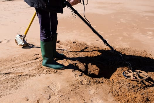 Person using metal detector on sandy beach for buried treasures.