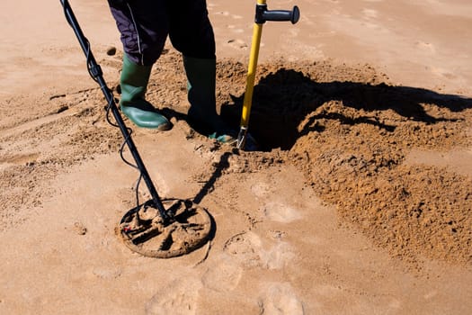 Metal detector enthusiast digging treasure on sandy beach.