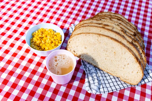 Sliced bread with corn and coffee on picnic tablecloth.