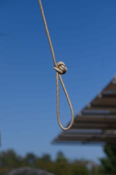 A tightly secured knot dangles from a rope, contrasting beautifully with the vibrant blue sky. Below, architectural elements gently frame the simplicity of the moment, evoking tranquility.